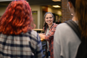 Happy female students talking in school hallway during break