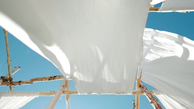 White linen cloth on wooden poles swings in the wind. Against the blue sky and green trees and fields.