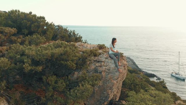 Woman sits on a boulder and watches seascape