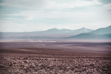Car speeds across the dusty plains next to the 'Laguna Colorada' in Bolivia, famous for its red lagoon water and flamingoes