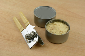 Two cans of albacore tuna fish with manual can opener on wooden table