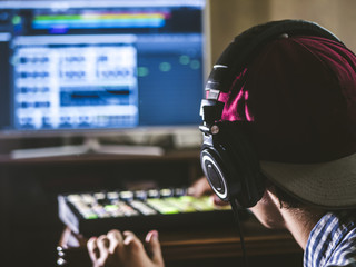 back view of sound engineer in snapback and holding headphones on head monitoring music in studio