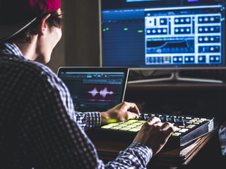 young male sound engineer working in professional music studio with modern equipment recording new...