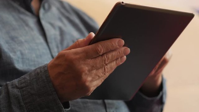 An Elderly Man Is Using Tablet Computer Sitting On The Couch