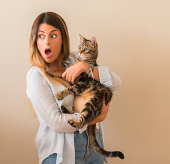 Young beautiful woman shocked with surprise face cuddling cat with love at home.