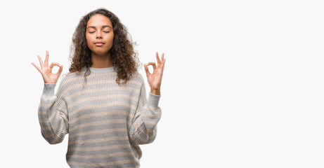 Beautiful young hispanic woman wearing stripes sweater relax and smiling with eyes closed doing meditation gesture with fingers. Yoga concept.