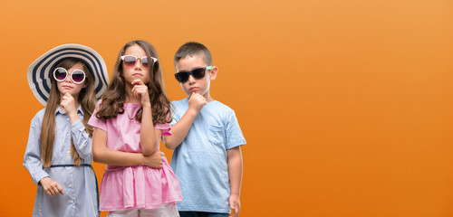 Group of boy and girls kids over orange background serious face thinking about question, very...