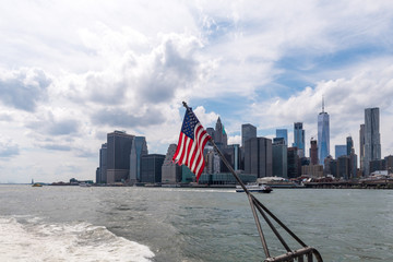 An American flag waves on the back of a ferry boat looking towards the downtown skyline of...