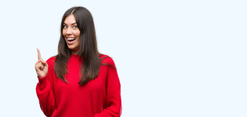 Young beautiful hispanic wearing red sweater pointing finger up with successful idea. Exited and...