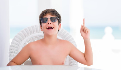 Young child on holidays sitting on a chair by the beach surprised with an idea or question pointing...