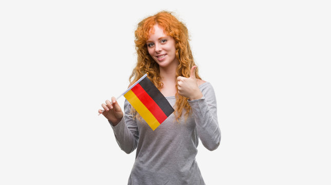 Young redhead woman holding flag of Germany happy with big smile doing ok sign, thumb up with fingers, excellent sign
