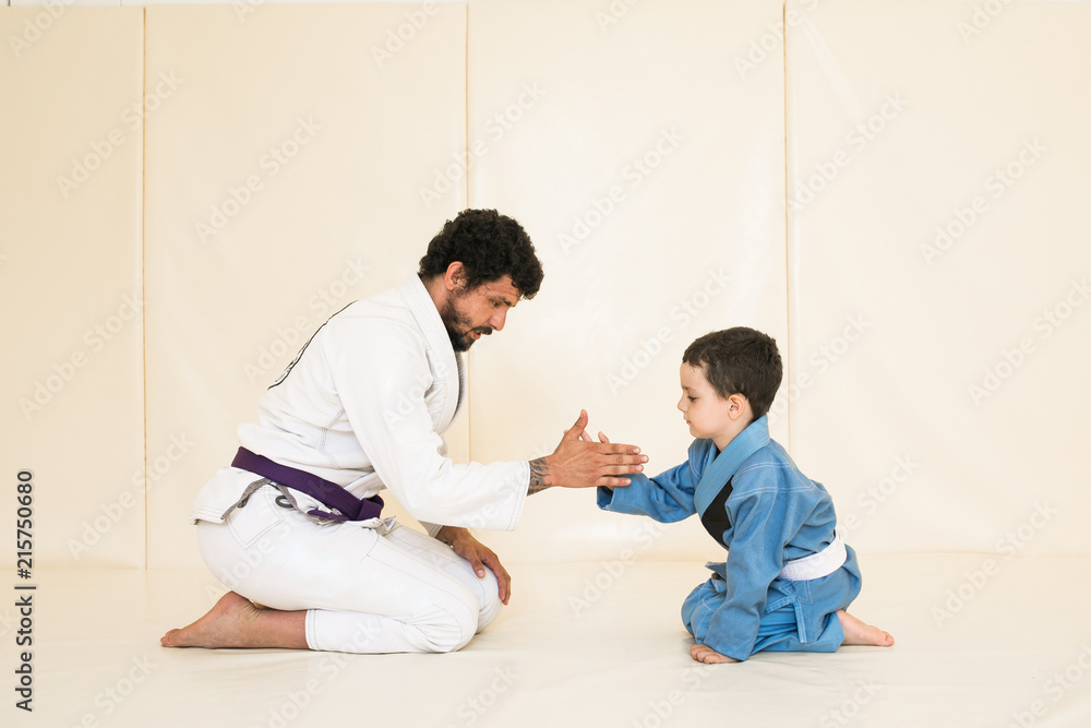 Wall mural father and little kid son are engaged in wrestling jiu-jitsu in the gym in a kimono. trainer teaches