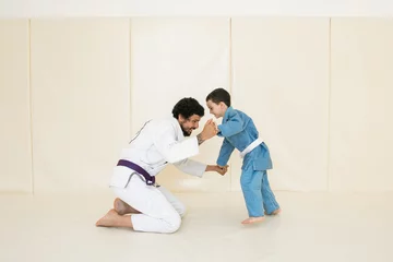 Photo sur Aluminium Arts martiaux Father and little kid son are engaged in wrestling jiu-jitsu in the gym in a kimono. Trainer teaches child the methods and positions of single combat, karate or aikido.