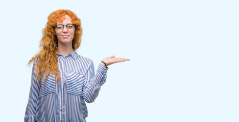 Young redhead bussines woman smiling cheerful presenting and pointing with palm of hand looking at...