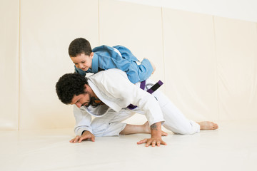 Father and little kid son are engaged in wrestling jiu-jitsu in the gym in a kimono. Trainer...