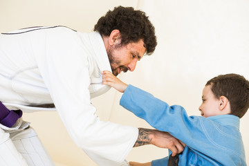Obraz premium Father and little kid son are engaged in wrestling jiu-jitsu in the gym in a kimono. Trainer teaches child the methods and positions of single combat, karate or aikido.