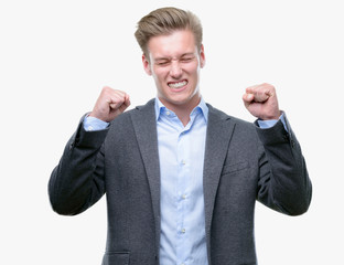 Young handsome blond business man excited for success with arms raised celebrating victory smiling. Winner concept.