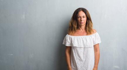 Middle age hispanic woman standing over grey grunge wall with serious expression on face. Simple and natural looking at the camera.
