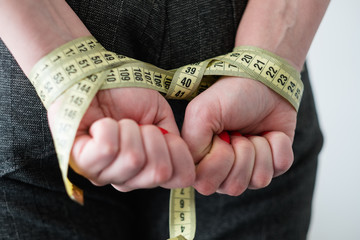 food deficiency. strict weightloss diet. unhealthy slimming methods. woman hands tied with measuring tape behind her back
