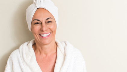 Beautiful middle age woman, wet hair wearing a towel with a happy face standing and smiling with a...