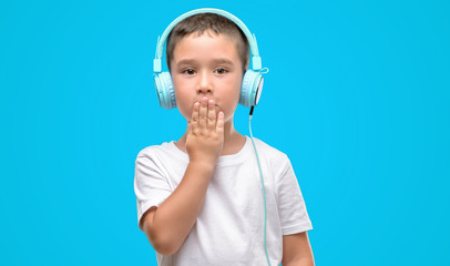 Dark haired little child listening music with headphones cover mouth with hand shocked with shame for mistake, expression of fear, scared in silence, secret concept
