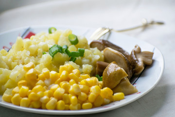 Fried potatoes with cepes and corn in a plate on the table. Fried potatoes with pickled mushrooms and corn.