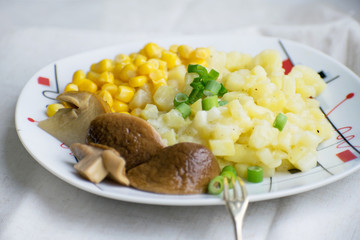 Fried potatoes with cepes and corn in a plate on the table. Fried potatoes with pickled mushrooms and corn.