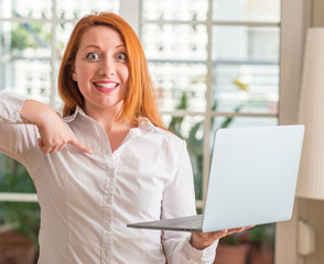 Redhead woman using computer laptop at home with surprise face pointing finger to himself