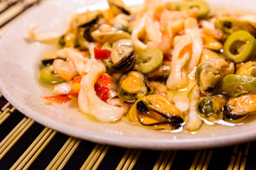 Ceramic plate with different sea food and olives on a bamboo mat