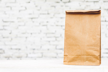 Blank paper bag with copy space for your brand on table against white brick wall background