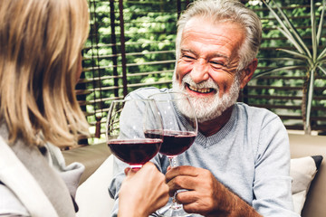 Senior couple relax talking and drinking wine glasses together on sofa in living room at...
