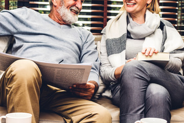Senior couple relax talking and reading newspaper together on sofa in living room at...