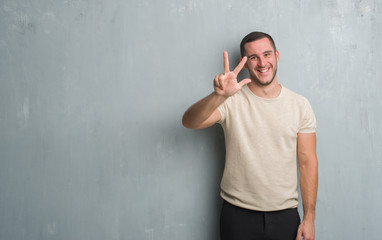 Young caucasian man over grey grunge wall showing and pointing up with fingers number three while...