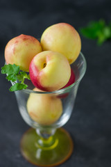 Ripe nectarines and mint leaves in a glass and nectarines on a dark background