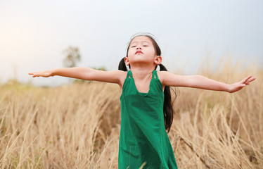 Asian Child girl closed eyes and outstretched arms in the dried grass field.