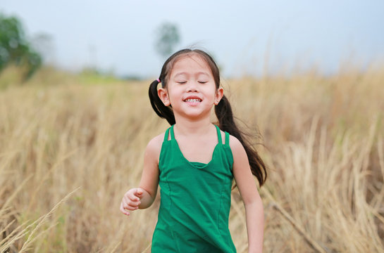 Happy Asian Child girl closed eyes and outstretched arms in the dried grass field.