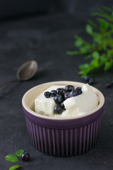 Ice cream with blueberries in a ceramic bowl, spoon and leaves scattered on a table