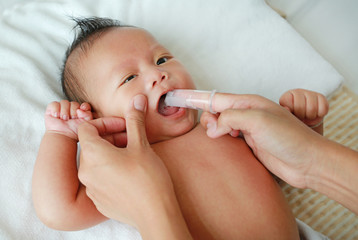 Mother hand clean baby tongue and gum with soft rubber brush.