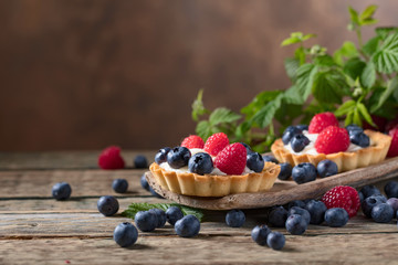  Dessert tarts with raspberries and blueberries on a wooden table.
