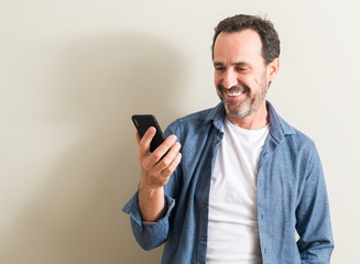 Senior man using smartphone with a happy face standing and smiling with a confident smile showing...