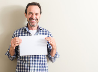 Senior man holding blank paper sheet with a happy face standing and smiling with a confident smile...