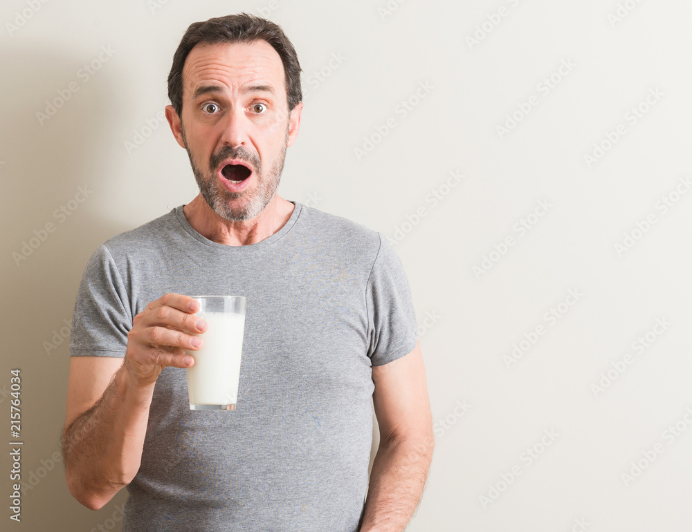 Sticker Senior man drinking a glass of milk scared in shock with a surprise face, afraid and excited with fear expression