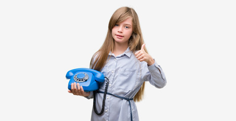 Young blonde toddler holding vintage telephone happy with big smile doing ok sign, thumb up with fingers, excellent sign