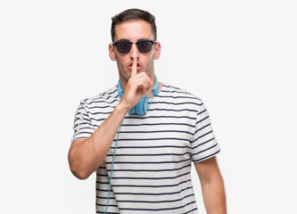 Handsome young man wearing headphones asking to be quiet with finger on lips. Silence and secret...