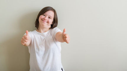Down syndrome woman standing over wall approving doing positive gesture with hand, thumbs up...