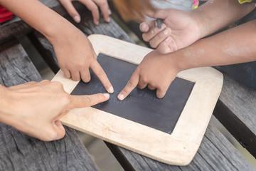 Children enjoy writing and drawing using a blackboard outdoor. Mother teach here little children to write on blackboard outdoor. Poor children using a small board for writing in countryside.