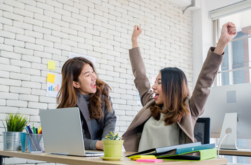 Two colleague businesswoman arms up for good news from job on laptop about work at office.Digital...