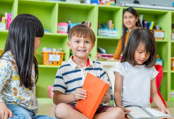 Children sitting on floor and reading tale book  in preschool library with teacher,Kindergarten school education concept.