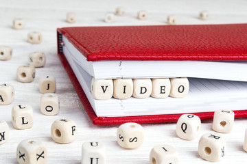 Word Video written in wooden blocks in red notebook on white wooden table.