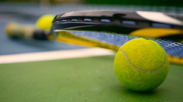 Close up of tennis equipment on the court. Sport, recreation concept. Yellow racket with a tennis ball in motion on a clay green blue court next to the white line with copy space and soft focus.